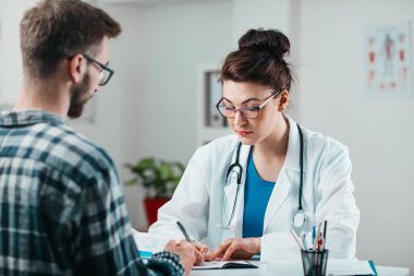 Kadın doktor, hastalığını tedavi etmesi için genç hastaya ilaç yazıyor.