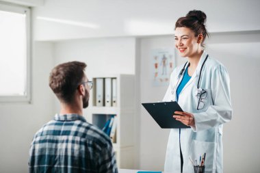 Kadın doktor hastalığını tedavi etmeden önce genç hastaya sonuçları okur.