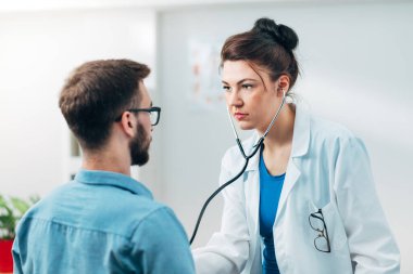Steteskop kullanan kadın doktor hastanın göğsünü kontrol ediyor.