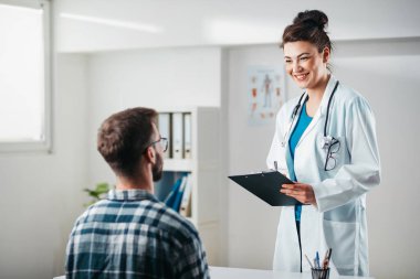 Kadın doktor hastalığını tedavi etmeden önce genç hastaya sonuçları okur.