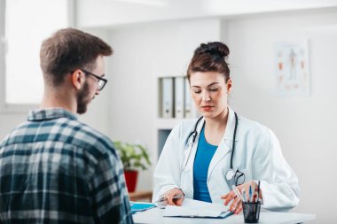 Kadın doktor, hastalığını tedavi etmesi için genç hastaya ilaç yazıyor.