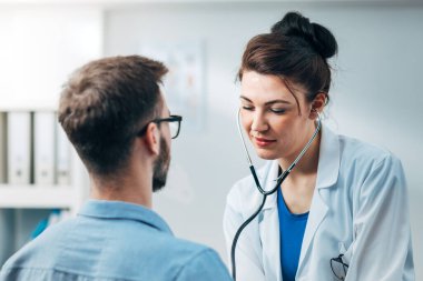 Steteskop kullanan kadın doktor hastanın göğsünü kontrol ediyor.