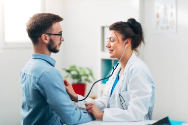 Steteskop kullanan kadın doktor hastanın göğsünü kontrol ediyor.