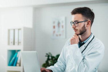 Laptop üzerinde çalışan genç doktorun portresi. Hastanedeki gönüllü, hastalıkların tedavisinde pratik bilgi kazanıyor