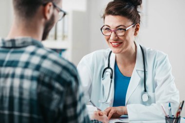 Kadın doktor, hastalığını tedavi etmesi için genç hastaya ilaç yazıyor.