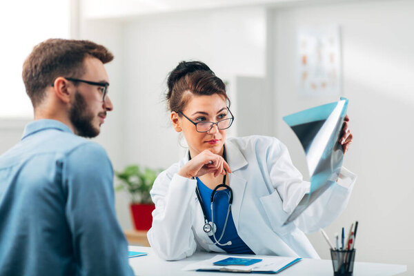 Портрет женщины-врача, сидящей в своем кабинете с пациенткой и смотрящей на рентген
