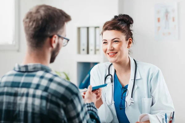 Kadın doktor, hastalığını tedavi etmesi için genç hastaya ilaç yazıyor.