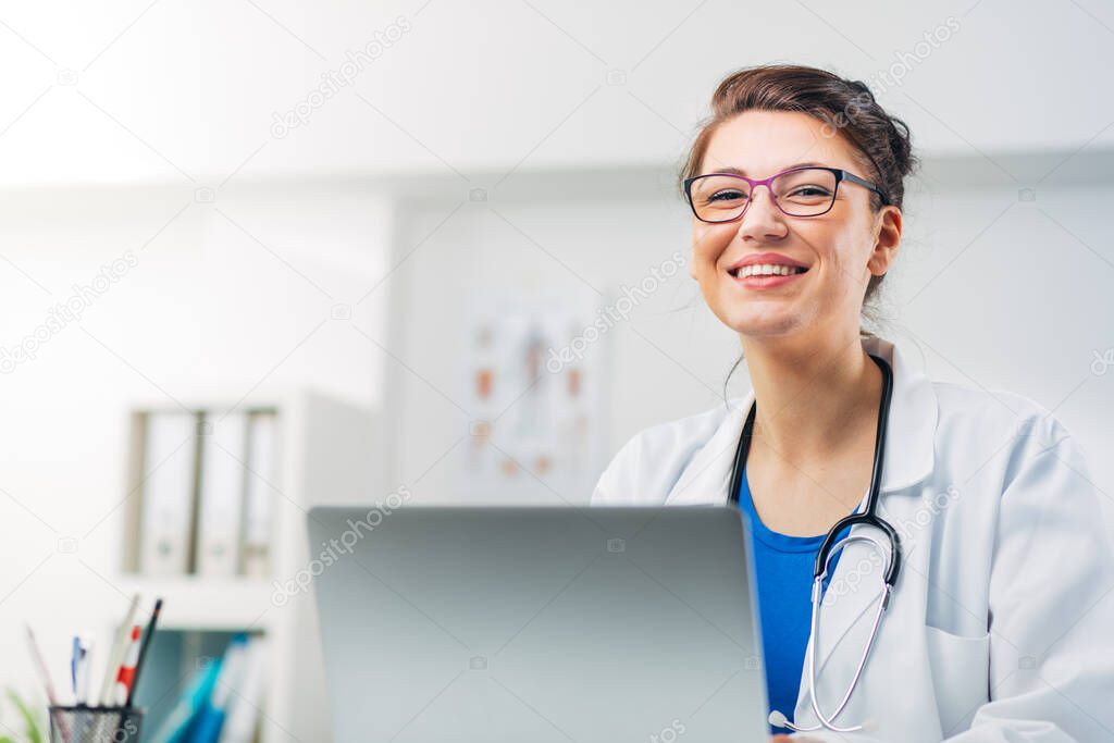 Portrait of Female Doctor sitting in her Medical Office with Stetoscope writing Prescription