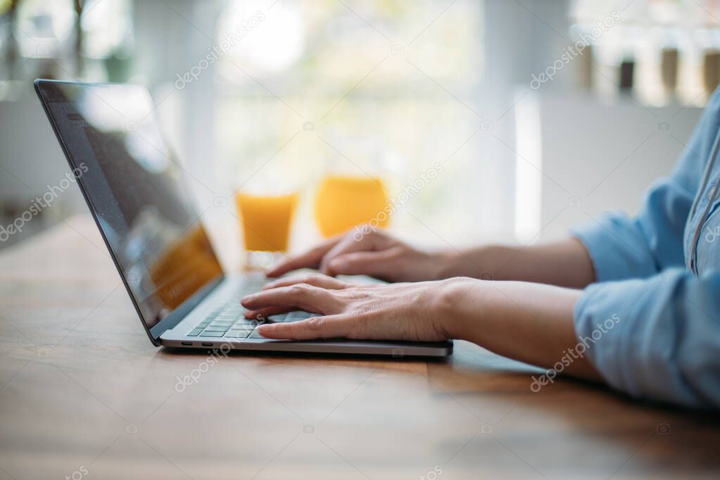 Detail of a woman typing on a laptop keyboard at home