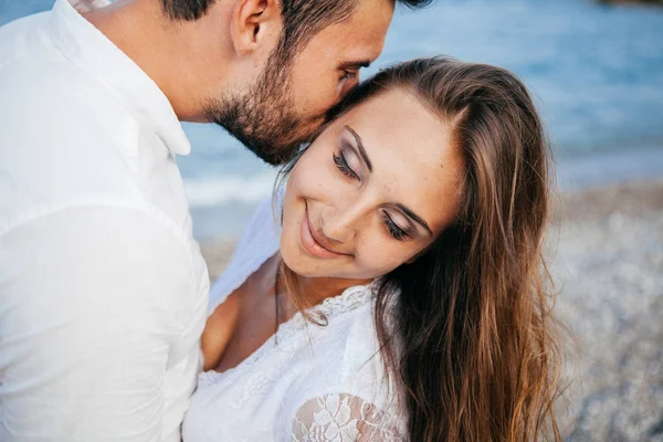 Boldog, fiatal pár, átfogó és átölelve, mosolyogva szerelmes a tengerparton — Stock Fotó