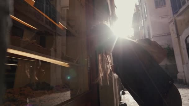 Touriste femme avec sac à dos se tient à la fenêtre de la boulangerie et regarde les bonbons, biscuits et petits pains affichés à l'intérieur — Video