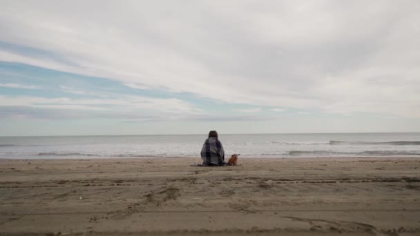 少女は海で、暖かい毛布に包まれ、本を読んで座っている。それから女は本を捨て、カベレー帽を落とし、海に走ります。後景 — ストック動画