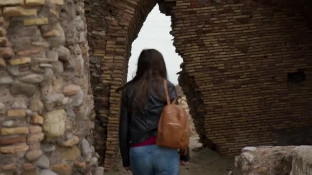 Toeristische meisje met een rugzak gaat door boog in ruïnes van een oude vesting Torre Flavia in Ladispoli, Italië. Achteraanzicht — Stockvideo