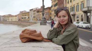 Genç çekici kız turist, İtalya 'nın antik Pisa kentinin tarihi binalarının arka planına karşı Arno nehrinin setinin kenarında duruyor.