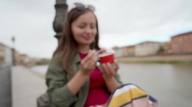 Gezinti güvertesinde oturmuş İtalyan dondurmasının tadını çıkaran genç bir kadın. Genç kız kameraya gülümsüyor ve lezzetli dondurmayla kaşık gösteriyor. Bulanık arkaplan