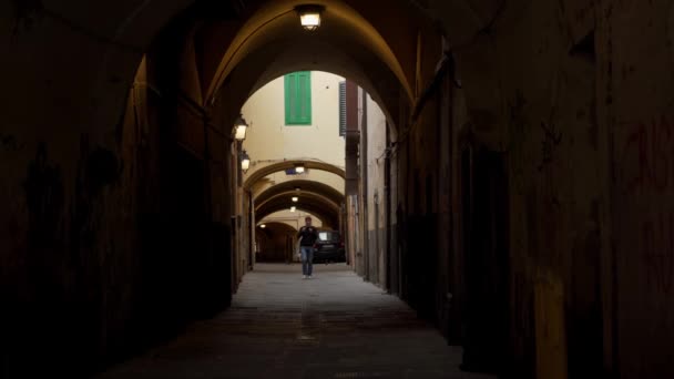 Молодой человек покидает двор дома через арку в европейском городе — стоковое видео