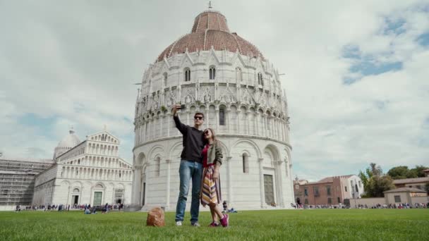 O par amoroso tira a autofoto pelo telefone inteligente contra o contexto de Batistério de São João, Pisa, Itália. Conceito de viagem — Vídeo de Stock