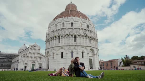 Pareja de amantes sentados soñando cerca del Baptisterio de San Juan, Plaza de los Milagros. Vacaciones italianas en Pisa. Un hito famoso. Vista general — Vídeos de Stock
