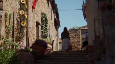 Girl in romantic dress travels through cozy street of Pienza old town. Rear view