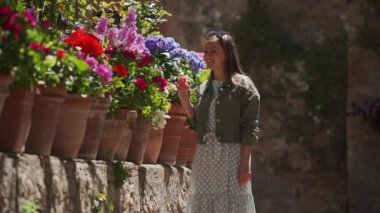 Happy girl in a romantic dress, jacket walks along flower bed and touches flower