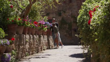 Pair of young people walk around old city holding hands along colored flower bed