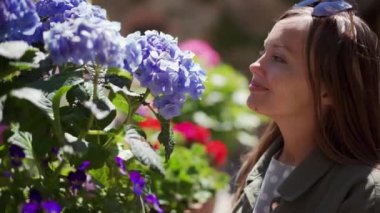 Happy girl with sunglasses looks at blue hydrangeas and smells flower. Sunny day