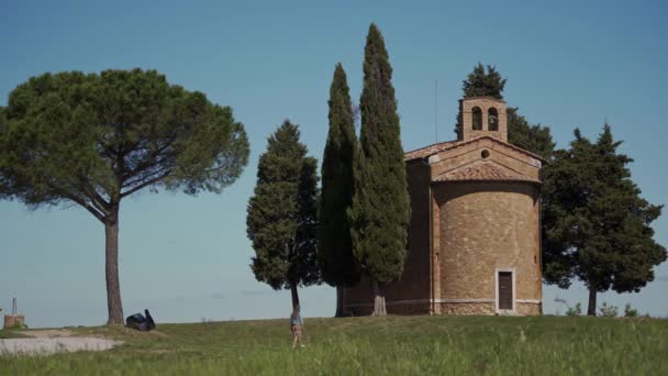 Chica en vestido va de gran árbol verde a la antigua capilla de piedra Cappella Vitaleta — Vídeos de Stock