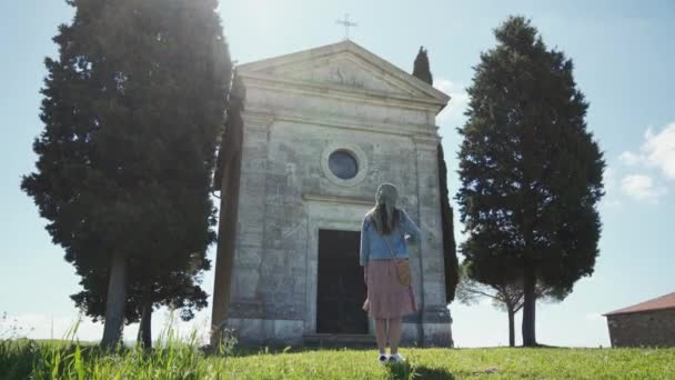 Woman in scarf stands near Cappella di Vitaleta, cross herself. Long shot, sunny — ストック動画