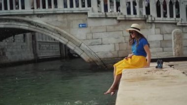 Şapkalı güzel kadın taş iskelede oturur ve çıplak ayaklarıyla su sıçratır.