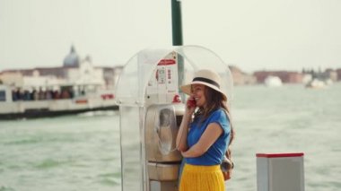 Hasır şapkalı kadın Grand Canal Seddi 'nde eski bir ankesörlü telefonla konuşuyor.