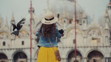 Şapkalı mutlu turist güvercinlerle oynuyor, onları besliyor, San Marco 'da eğleniyor.