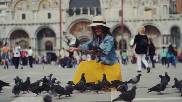 VENICE, ITALY - MAY 21, 2019: Girl in hat sits on San Marco square feeds pigeons — Stock Video