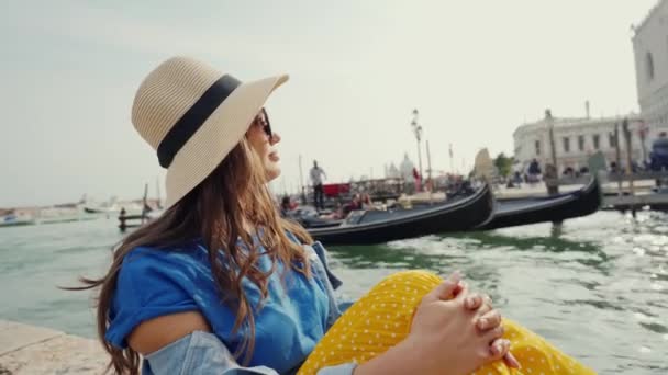 Ragazza carina in occhiali da sole, cappello siede sul molo, guarda gondole con i turisti — Video Stock