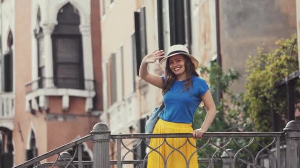 Cute girl in hat stands on bridge in romantic Venice, waves goodbye, leave frame — Stock Video