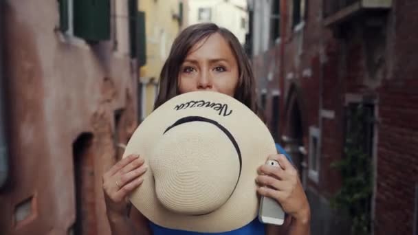 Morena chica de pie en la estrecha calle de Venecia, cubriendo su cara con sombrero de paja — Vídeo de stock