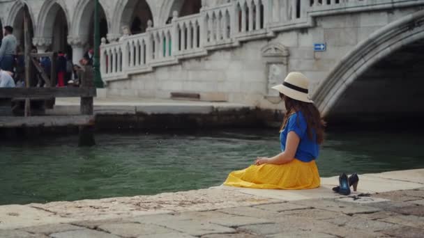 Venedig, Italien - 21 maj 2019: Kvinna i hatt sitter på piren, stänk vatten efter ben — Stockvideo