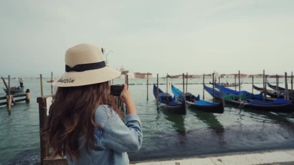 Женщина в шляпе фотографирует гондолы на Гранд-канале, делает селфи против лодок — стоковое видео