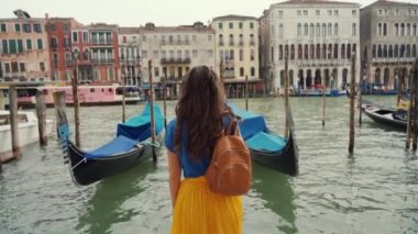 Kıvırcık esmer kız ayakta duruyor, kartpostal manzaralı gondollara bakıyor, Grand Canal 'da. Arka görünüm