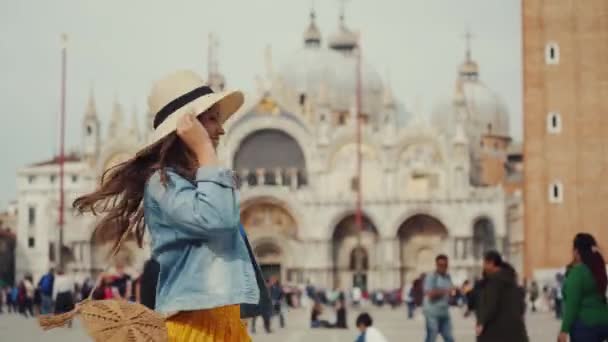 Lány kalap, farmer, sárga szoknya örvénylik a téren ellen elmosódott San Marco templom — Stock videók