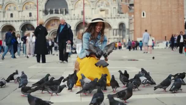 Venedig, Italien - 21 maj 2019: Kvinna i hatt sitter på berömda torget, matar duvor — Stockvideo