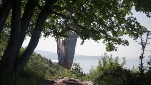 Hamaca vacía colgando de un árbol. Acogedor lugar para relajarse, vista panorámica del lago de Garda — Vídeos de Stock