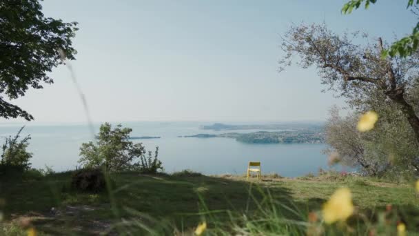 이탈리아에서 가장 큰 호수인 가르다 호수가 내려다 보이는 언덕에 있는 외로운 노란 의자 — 비디오