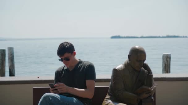 GARDONE RIVIERA, ITALY - MAY 23, 2019: guy poses like statue sitting on bench, — Stock Video