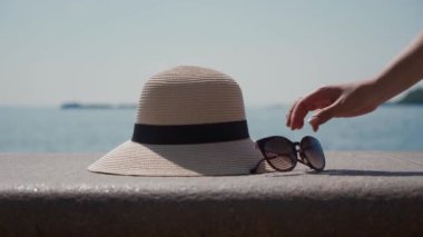 Kadın eli sırayla güneş gözlüğü ve hasır şapkayı çerçeveden çıkarır. Deniz Burnu