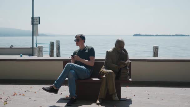 GARDONE RIVIERA, ITALY - MAY 23, 2019: man use phone sit on bench next to statue — Stock Video