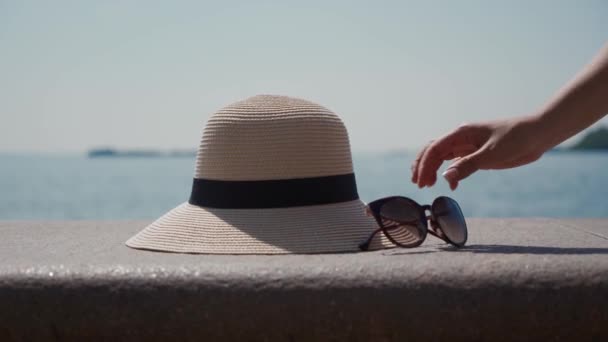 La mano femenina se turna para quitar las gafas de sol y el sombrero de paja del marco. Paisaje marino — Vídeos de Stock