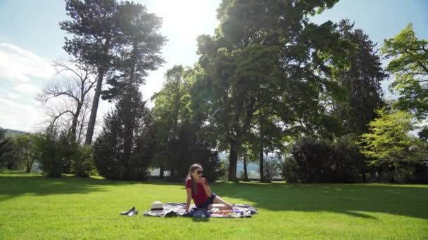 Mulher bonita em óculos de sol tem piquenique no dia ensolarado da primavera no cidade-parque — Vídeo de Stock