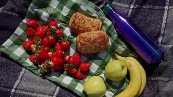 Piknikový ubrus na dece s čerstvým pekařstvím, jahodou, banánem, termoskou, sluncem — Stock video