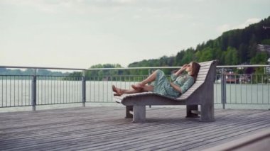 Romantik elbiseli esmer kadın, güneş gözlüklü. Gölün kenarında uzanmış dinleniyor.