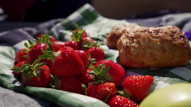 Close-up van picknickgerechten: aardbeien en verse bakkerij op tafellaken, zonnige dag — Stockvideo